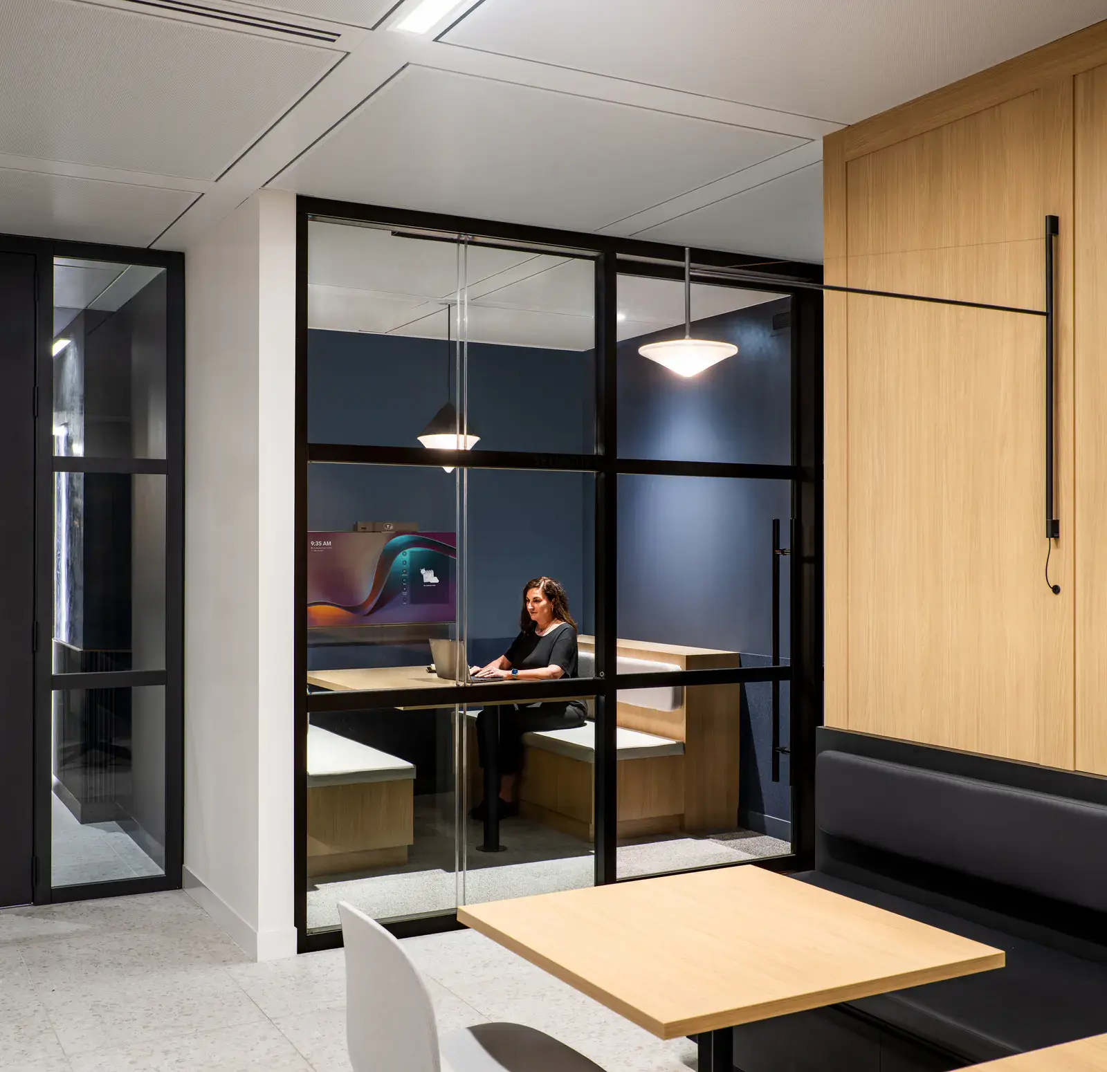 Person working in a glazed focus room beside an informal booth