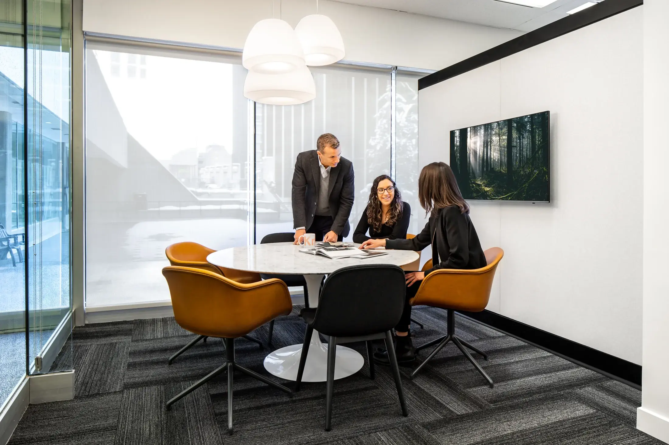 Three people collaborating around a table in a glazed meeting room